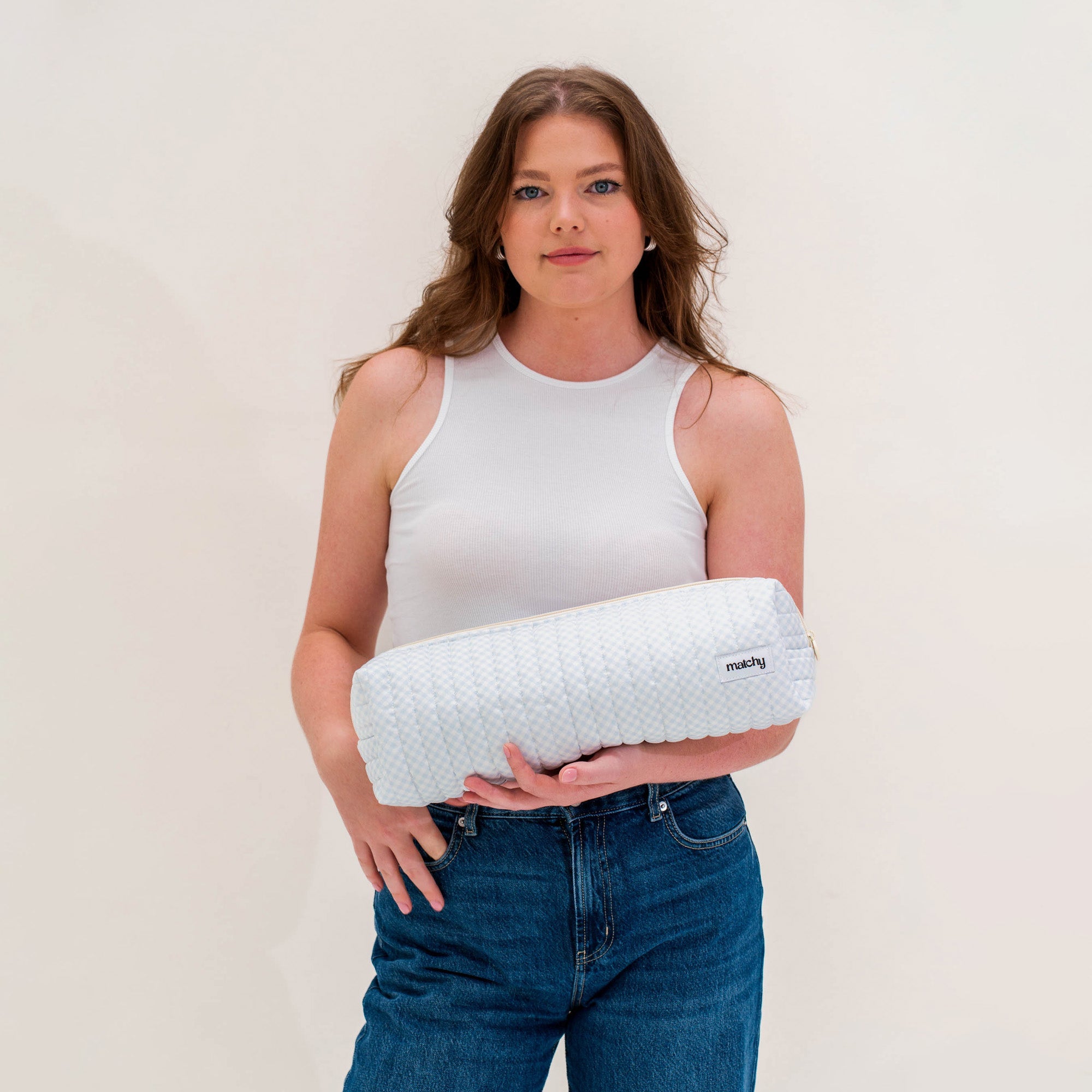 Woman in a white singlet and jeans holding a pale blue gingham quilted hair tools pouch. Matchy Blueberry Hair Tools Pouch.