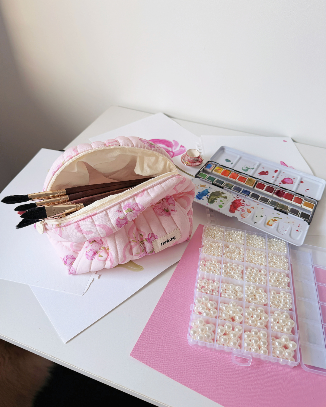 Open pink peony print carry-all bag holding paint brushes on a desk beside a watercolour palette and paper. Matchy Evermore Peony Carry-All Bag.