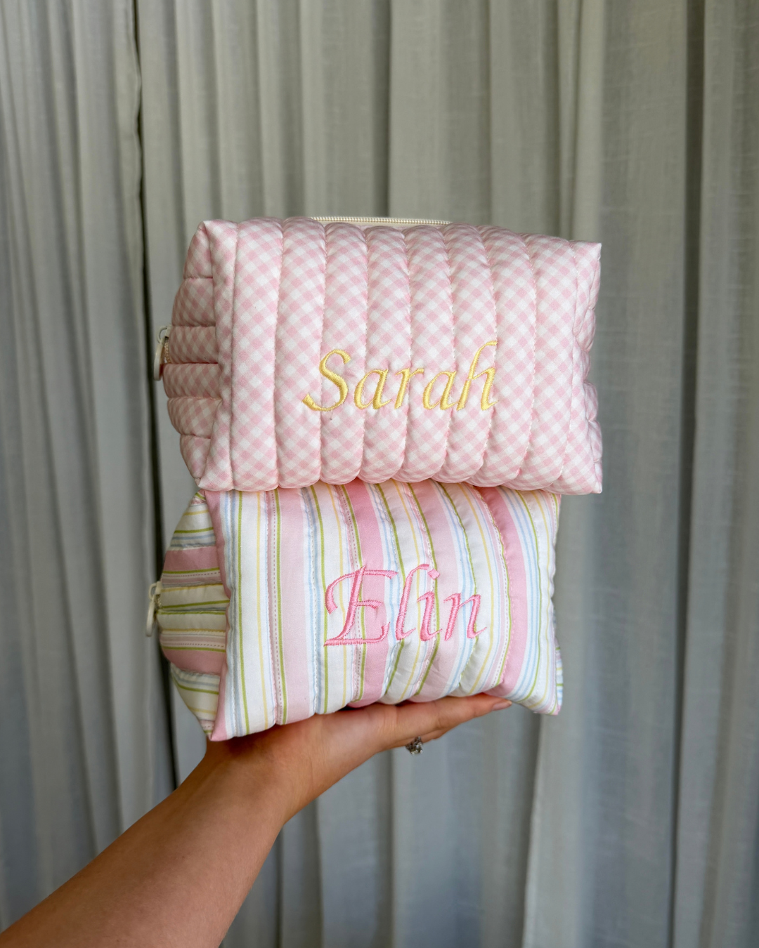 Hand holding two quilted carry-all bags, a pink gingham bag embroidered with 'Sarah' and a striped bag embroidered with 'Elin'. Matchy Strawberry Gingham Custom Embroidery Carry-All Bag.