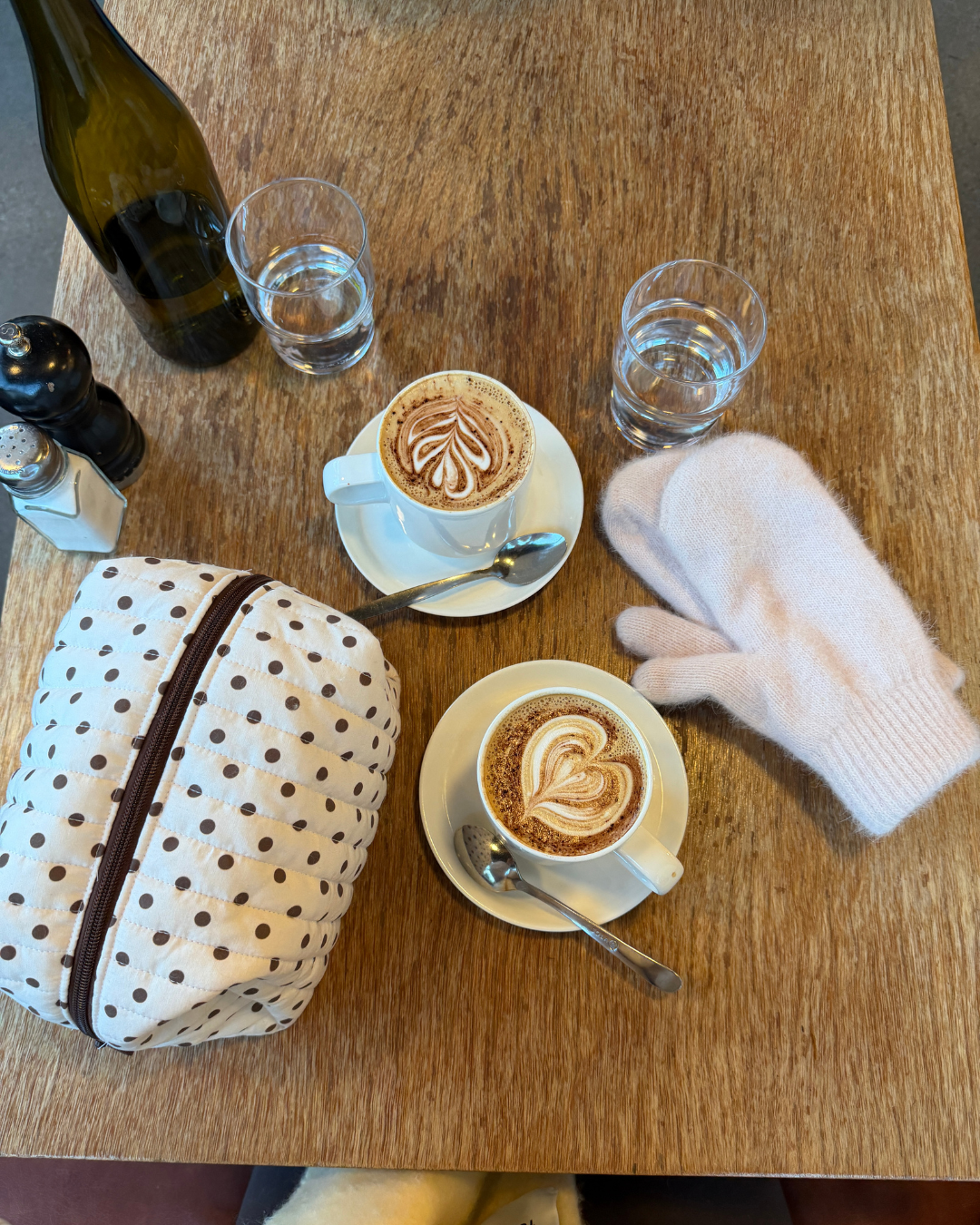 Cream and brown polka dot carry-all bag on a wooden cafe table next to two lattes and a pair of white mittens. Matchy Ken Carry-All Bag.
