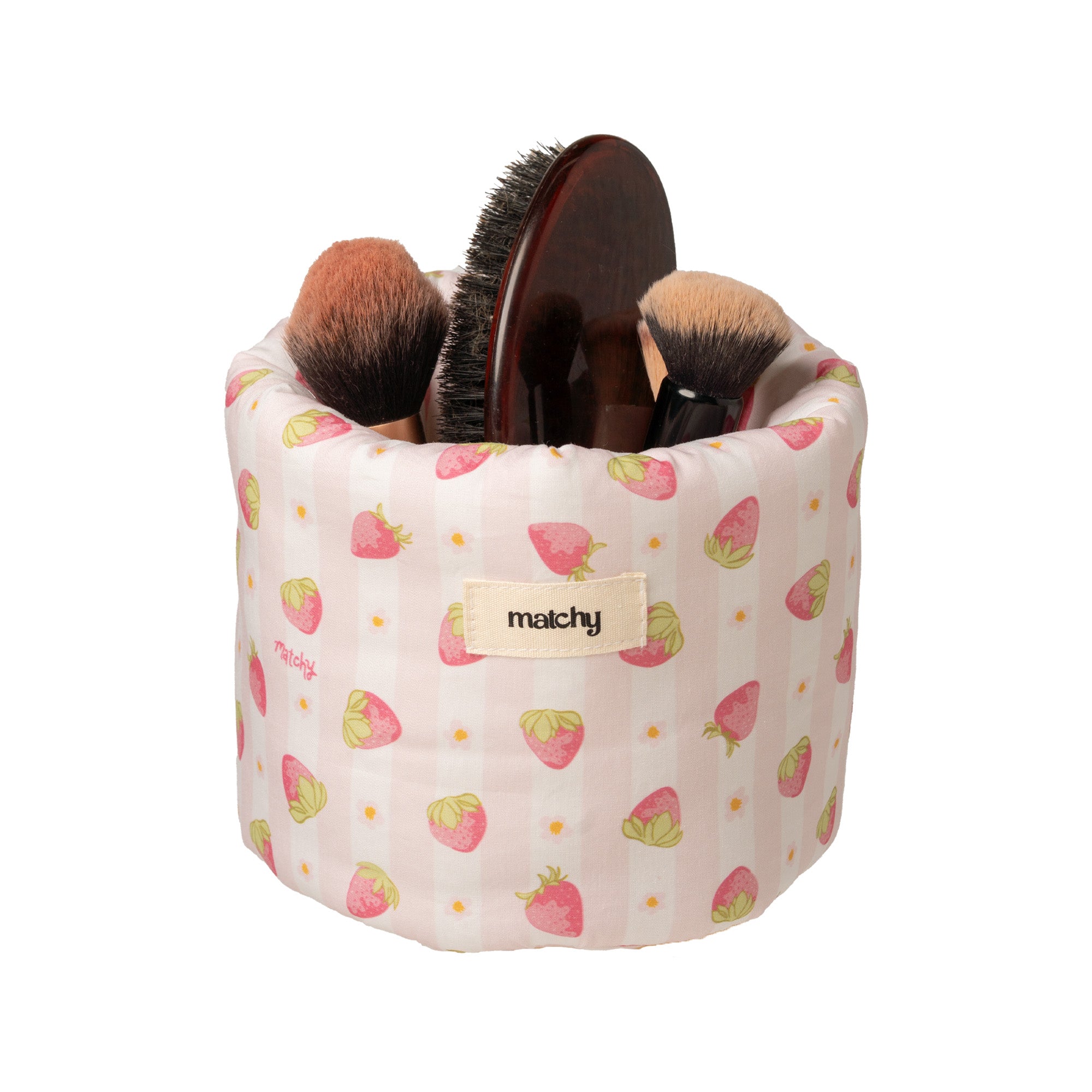 Pale pink strawberry print bubble bucket holding makeup brushes and a wooden hairbrush, with a 'matchy' label. Matchy Sylvie Bubble Bucket, a padded vanity storage bucket.