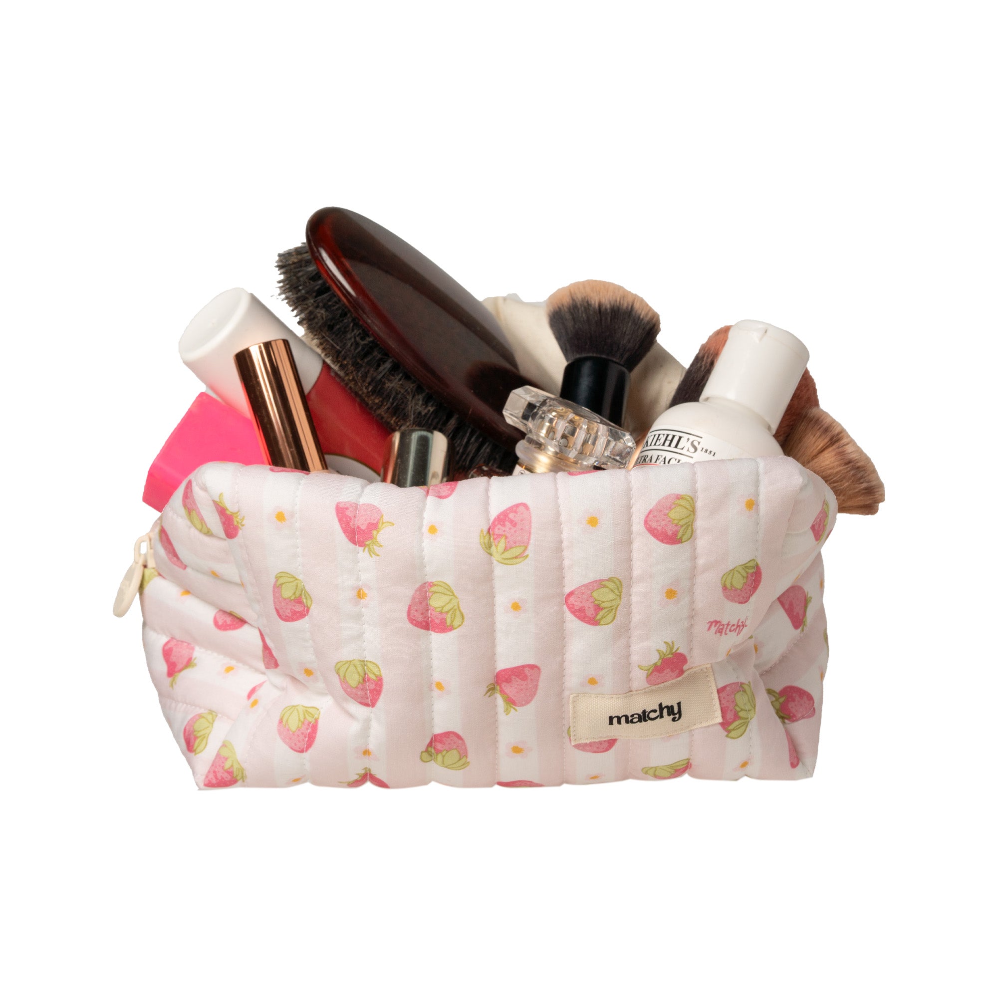 Pale pink strawberry print carry-all bag overflowing with makeup brushes, a hairbrush and skincare. Matchy Sylvie Carry-All Bag, a quilted makeup and toiletry bag.