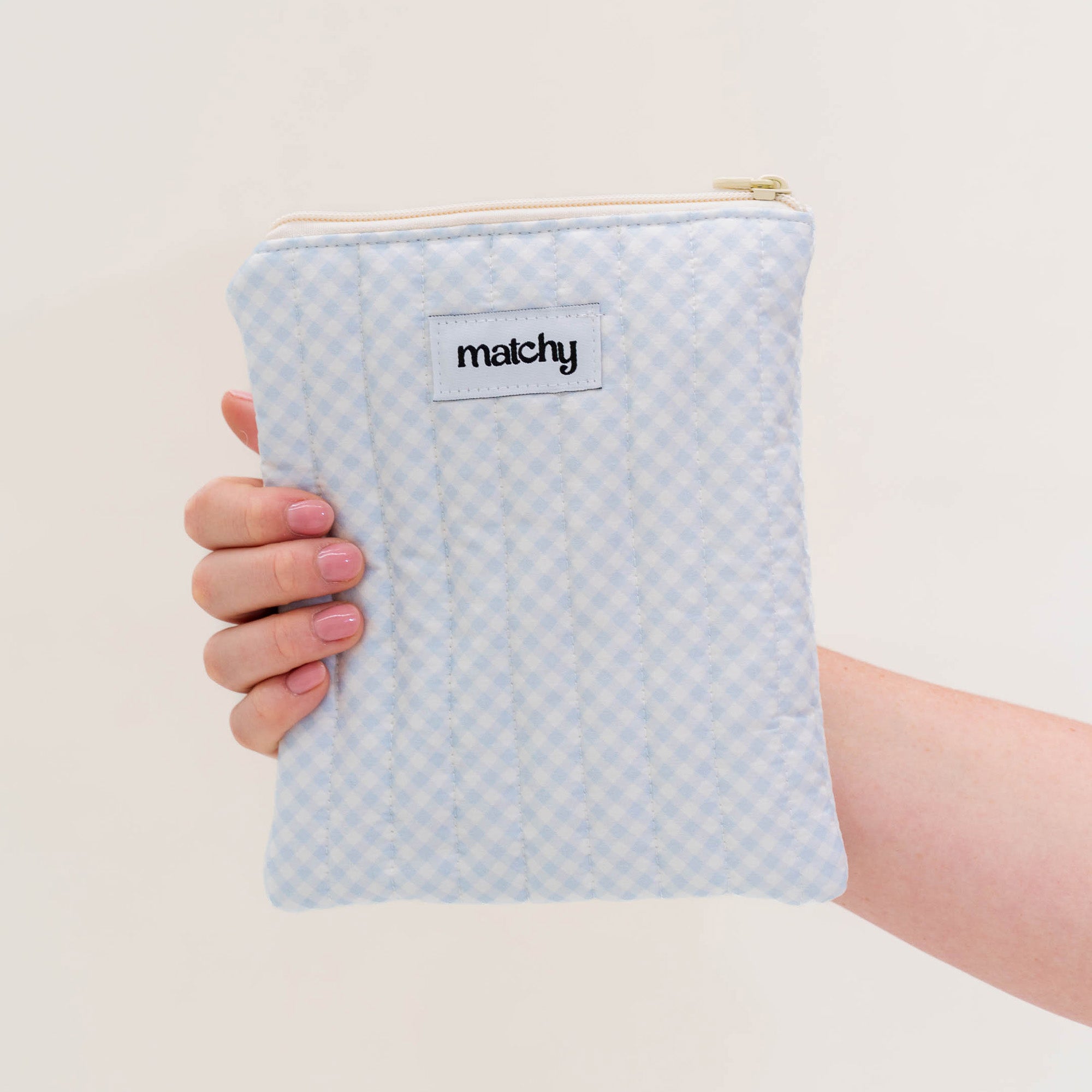 Hand holding a pale blue gingham quilted eReader sleeve with a 'matchy' label. Matchy Blueberry Gingham eReader Sleeve, a padded Kindle pouch.
