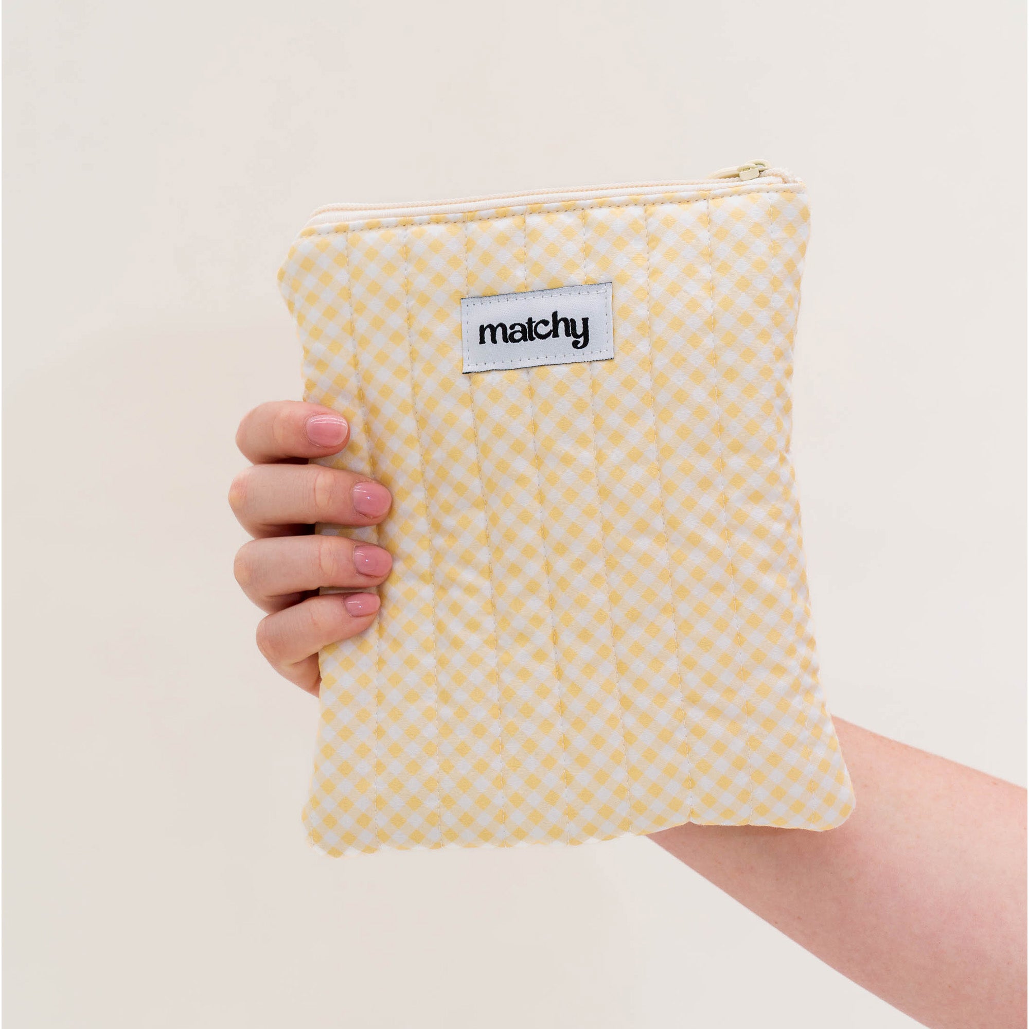 Hand holding a butter yellow gingham quilted eReader sleeve with a 'matchy' label. Matchy Banana Gingham eReader Sleeve, a padded Kindle pouch.