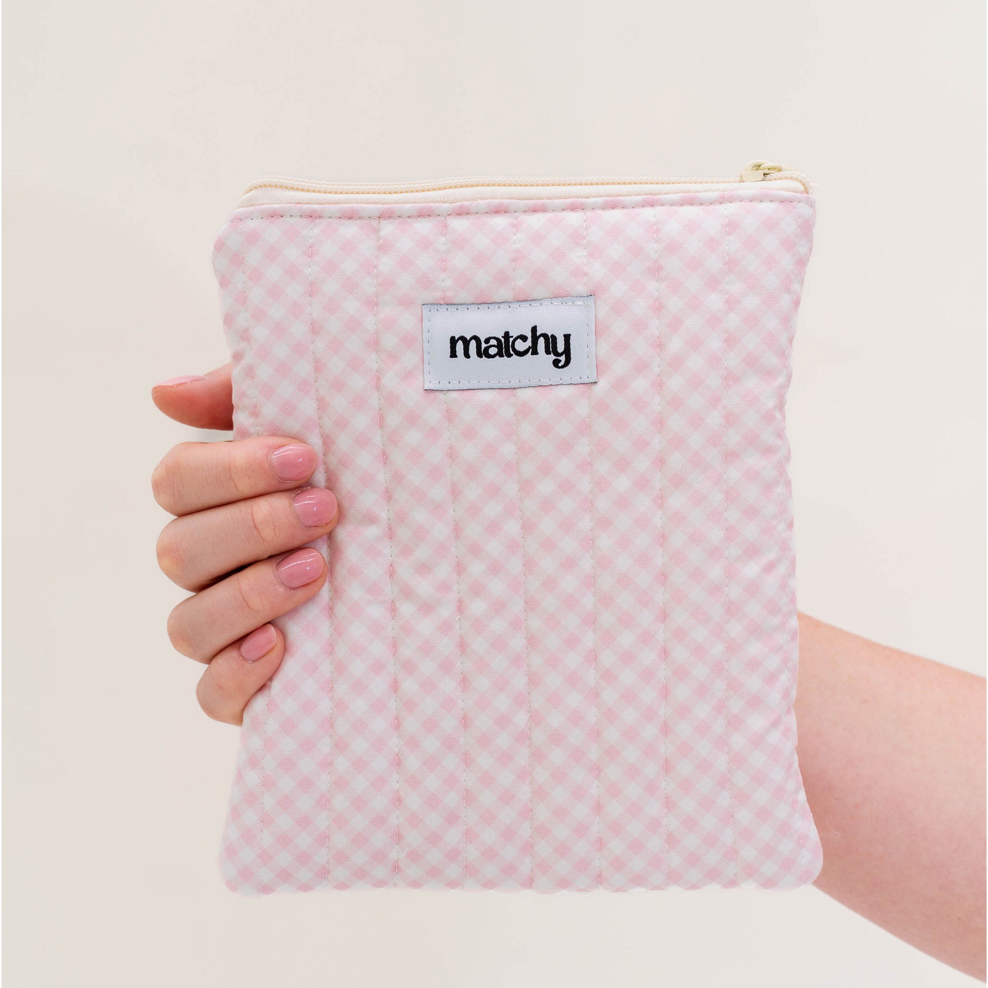 Hand holding a soft pink gingham quilted eReader sleeve with a 'matchy' label. Matchy Strawberry Gingham eReader Sleeve, a padded Kindle pouch.