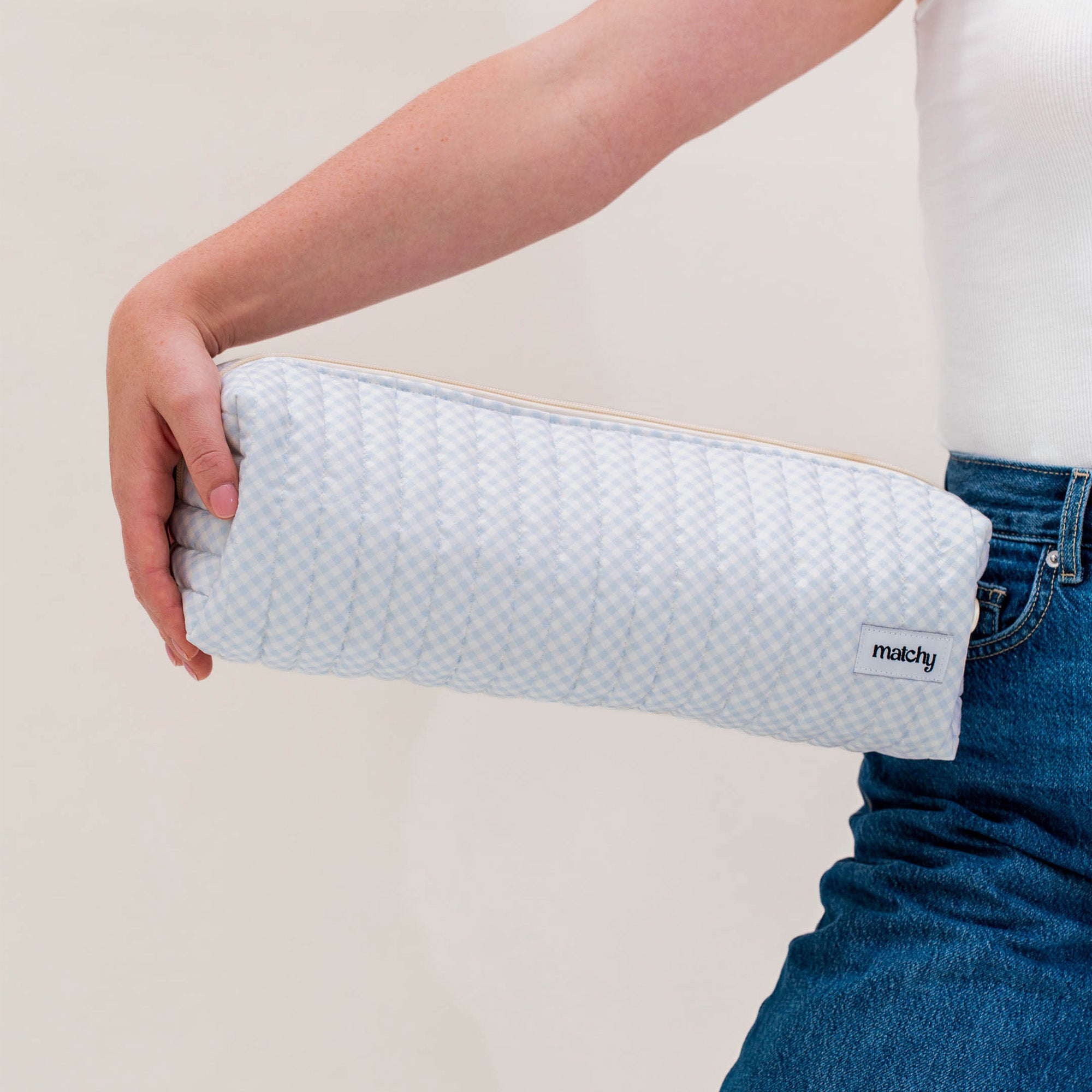 Woman holding a long pale blue gingham quilted pouch under her arm for size. Matchy Blueberry Hair Tools Pouch for straighteners and curling wands.
