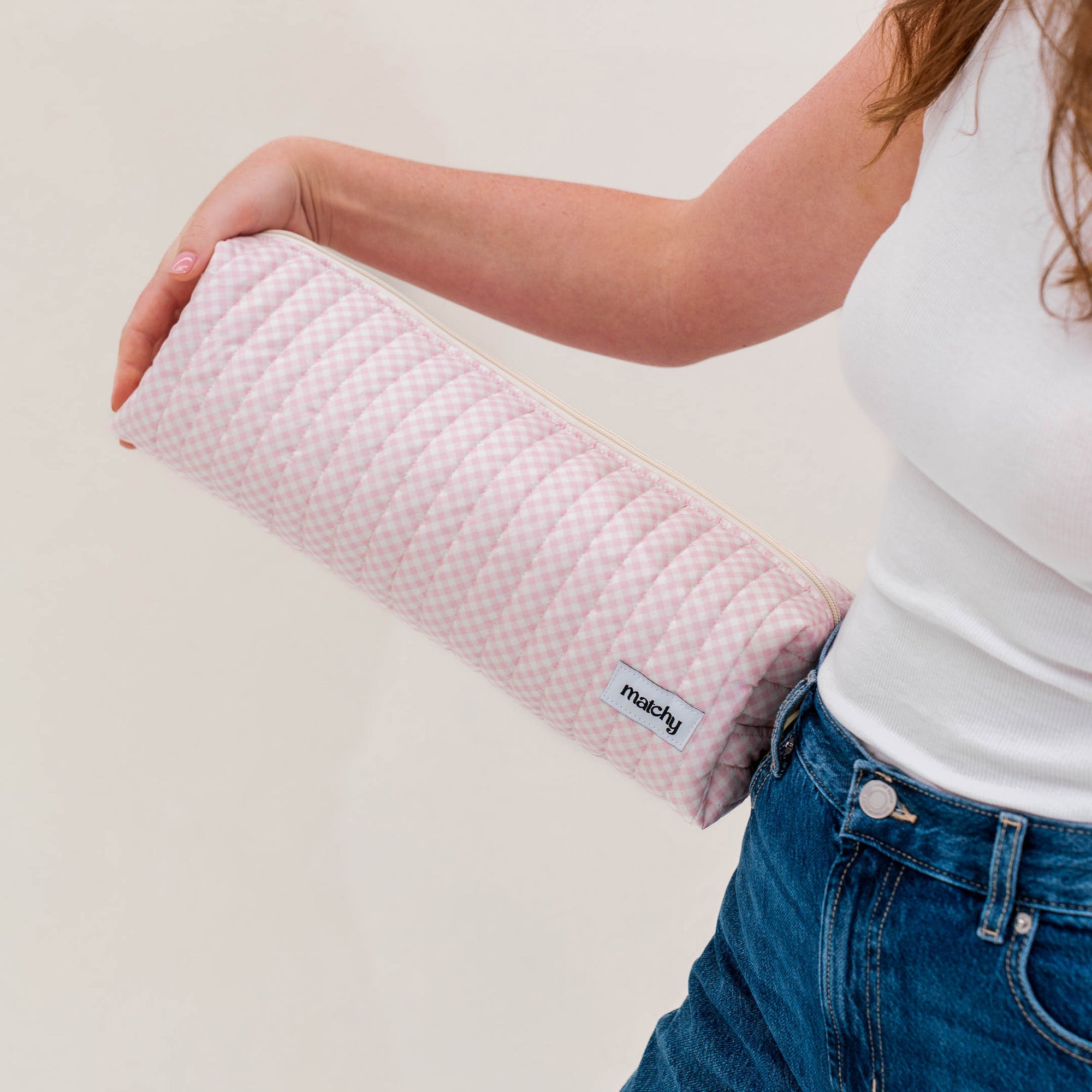 Woman holding a long soft pink gingham quilted pouch under her arm for size. Matchy Strawberry Hair Tools Pouch for straighteners and curling wands.