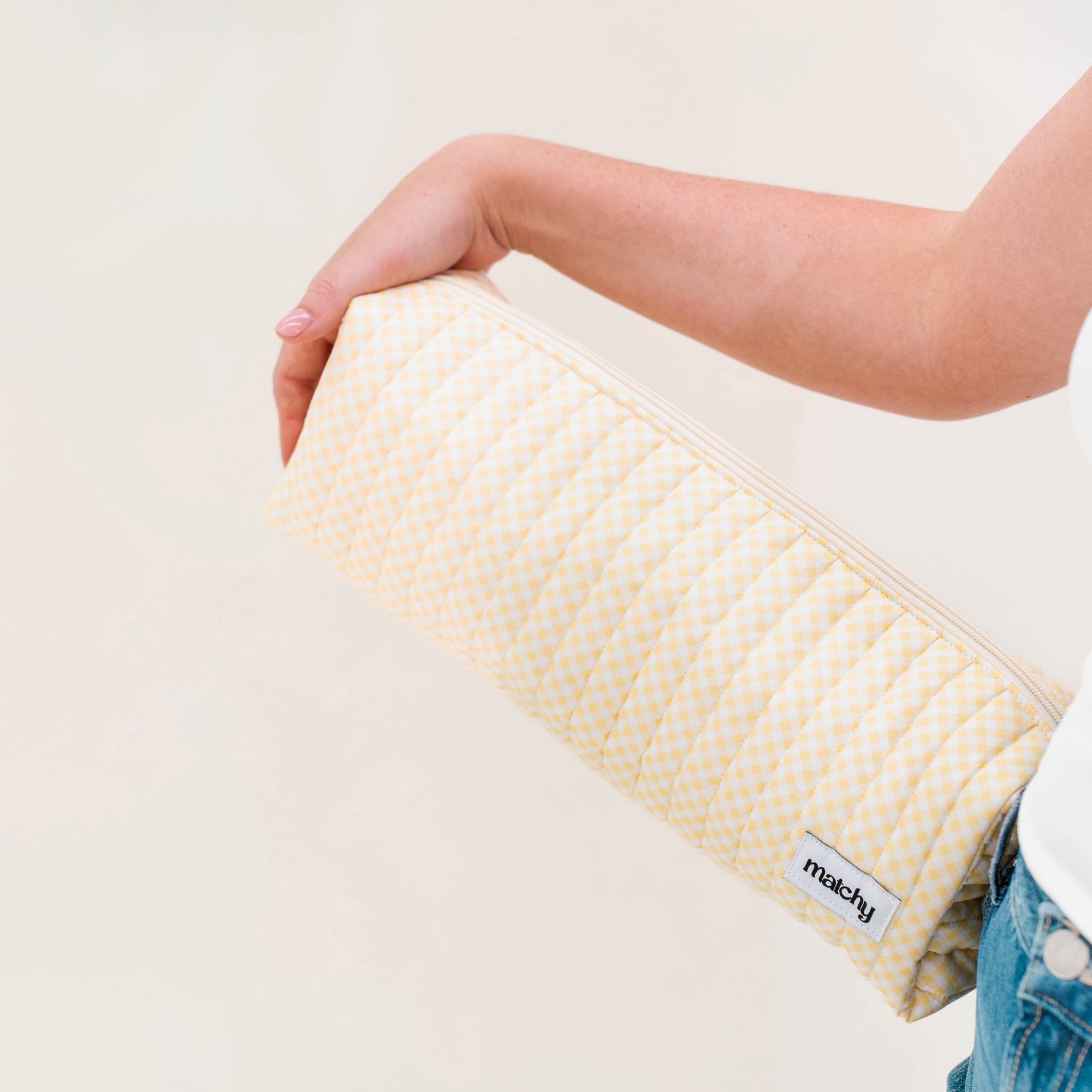 Woman holding a long butter yellow gingham quilted pouch for size. Matchy Banana Hair Tools Pouch for straighteners and curling wands.