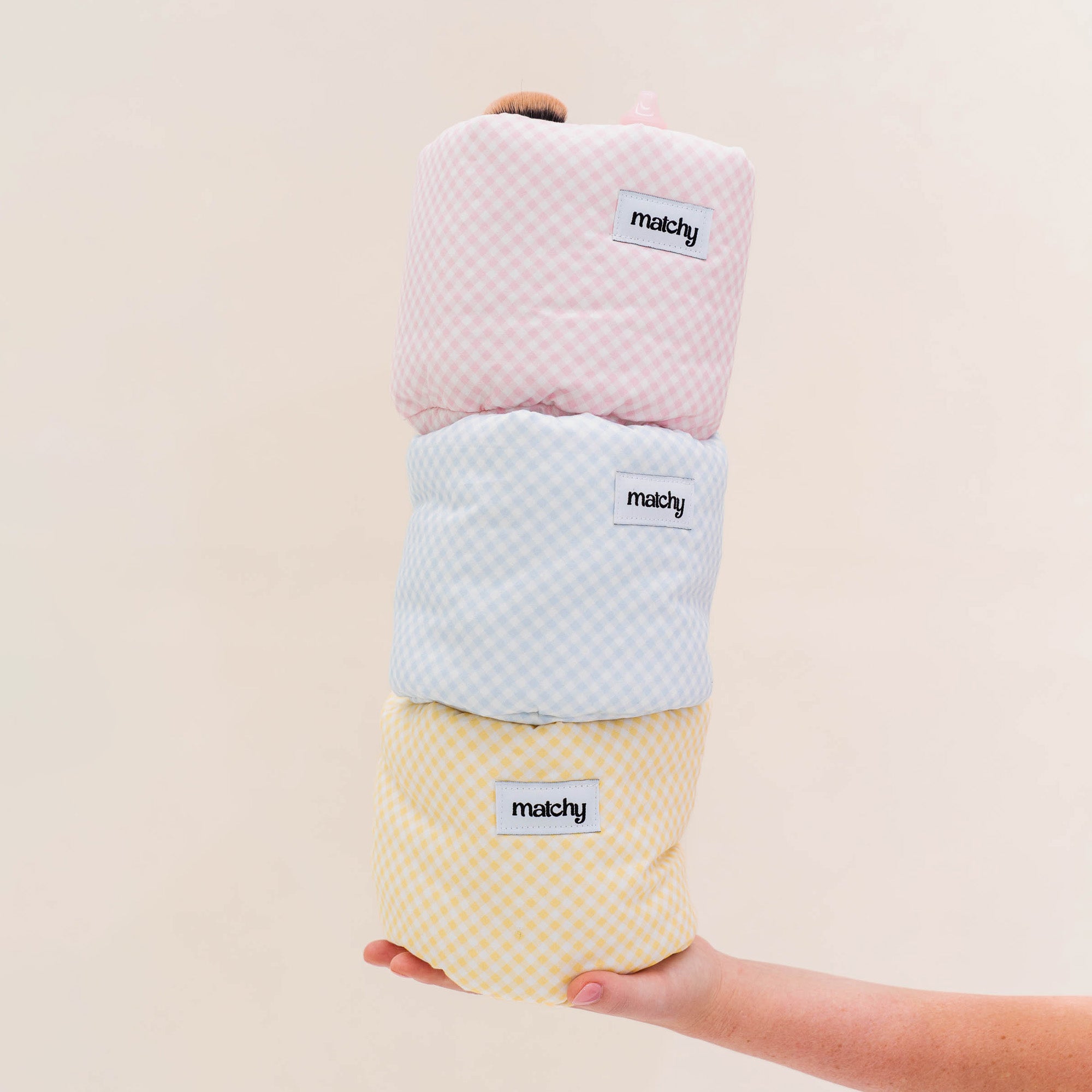 Hand balancing a stack of three gingham bubble buckets in pink, blue and yellow against a light background. Matchy Georgina Bubble Bucket in three colourways.