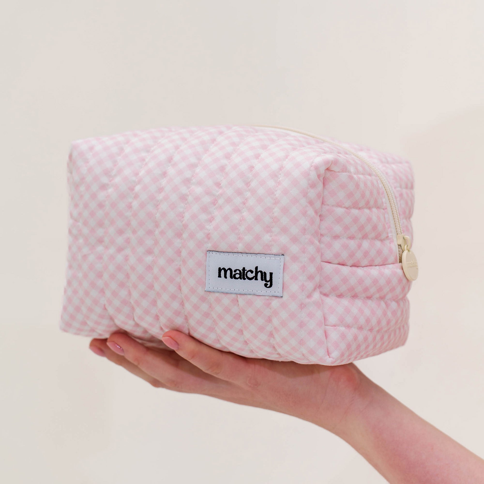 Hand holding a soft pink gingham quilted carry-all bag with a 'matchy' label. Matchy Strawberry Gingham Carry-All Bag.