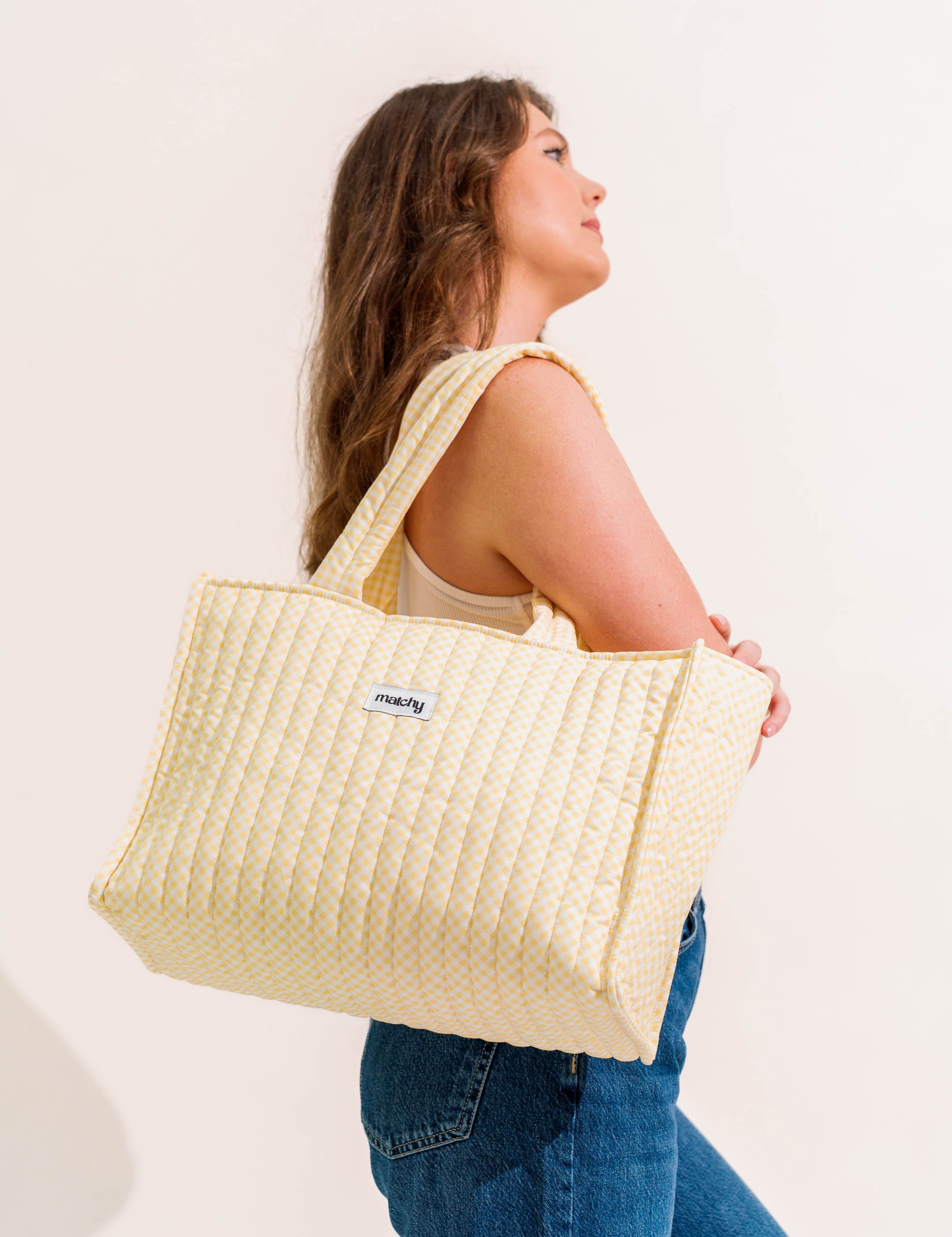 Woman in jeans carrying a butter yellow quilted tote bag over her shoulder. Matchy Banana Take Me With You Tote.