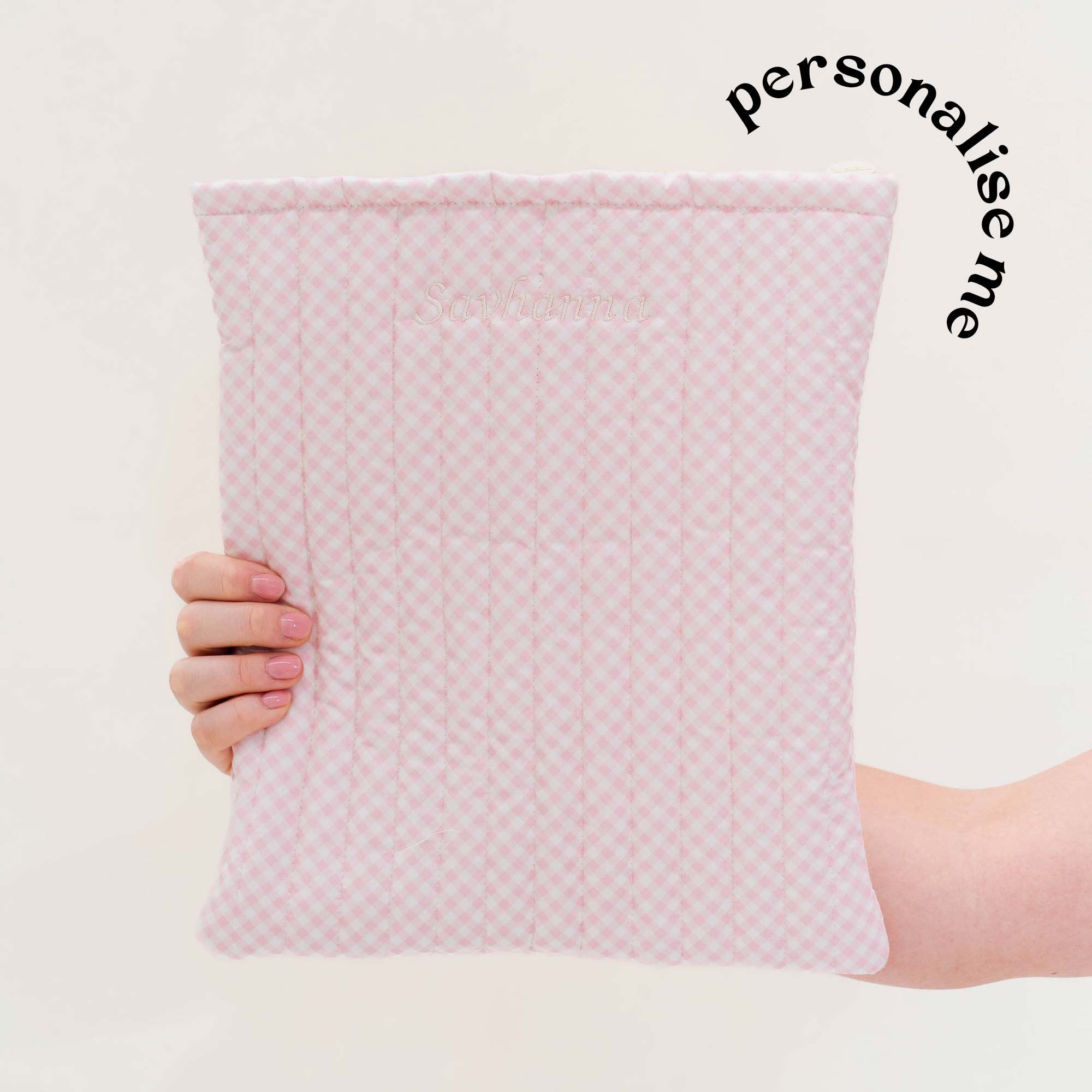 Hand holding a soft pink gingham quilted book sleeve with the words 'personalise me' curved beside it. Matchy Strawberry Gingham Custom Embroidery Book Sleeve.