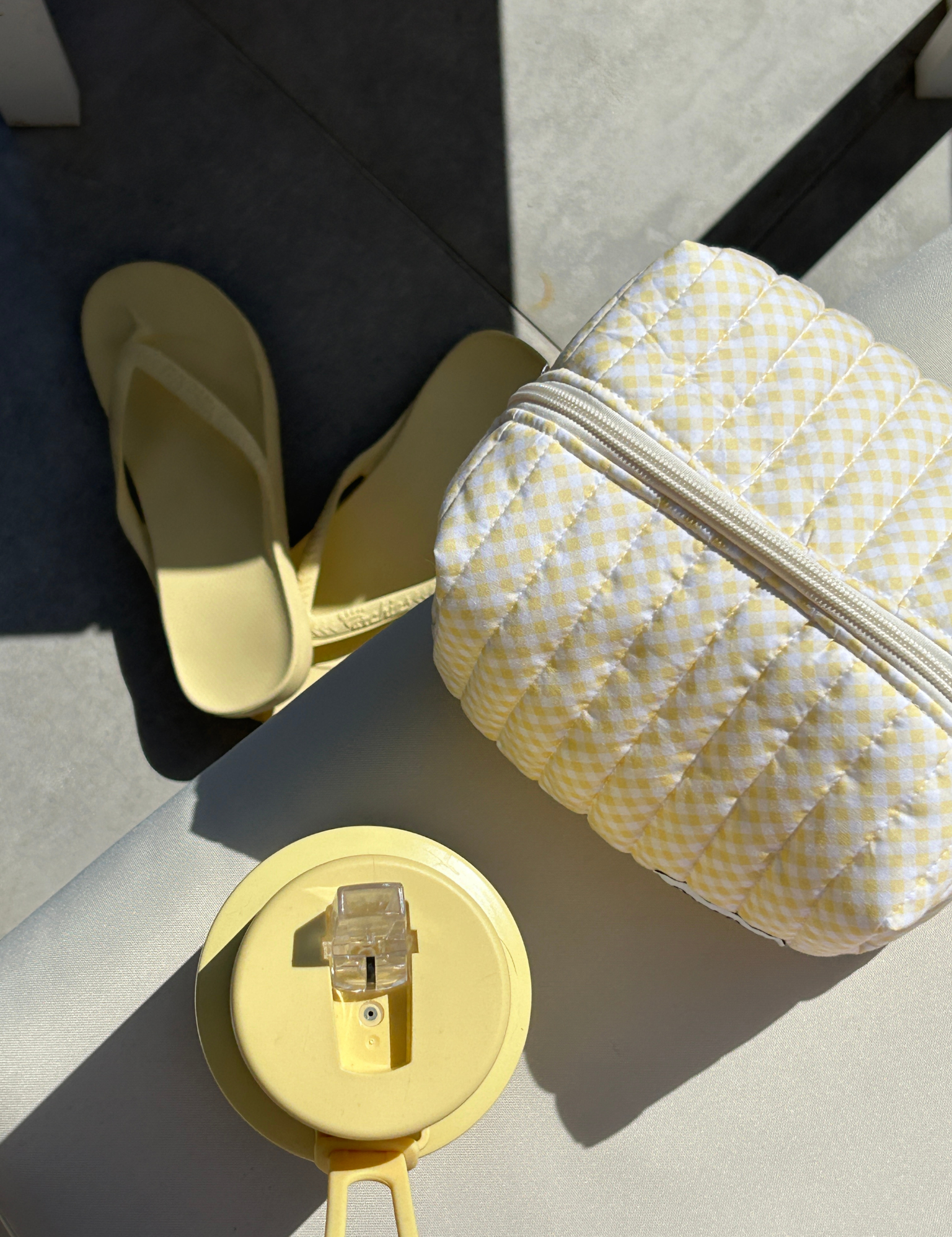 Butter yellow gingham quilted carry-all bag on a sunny tiled floor next to yellow thongs and a yellow drink bottle. Matchy Banana Gingham Carry-All Bag.