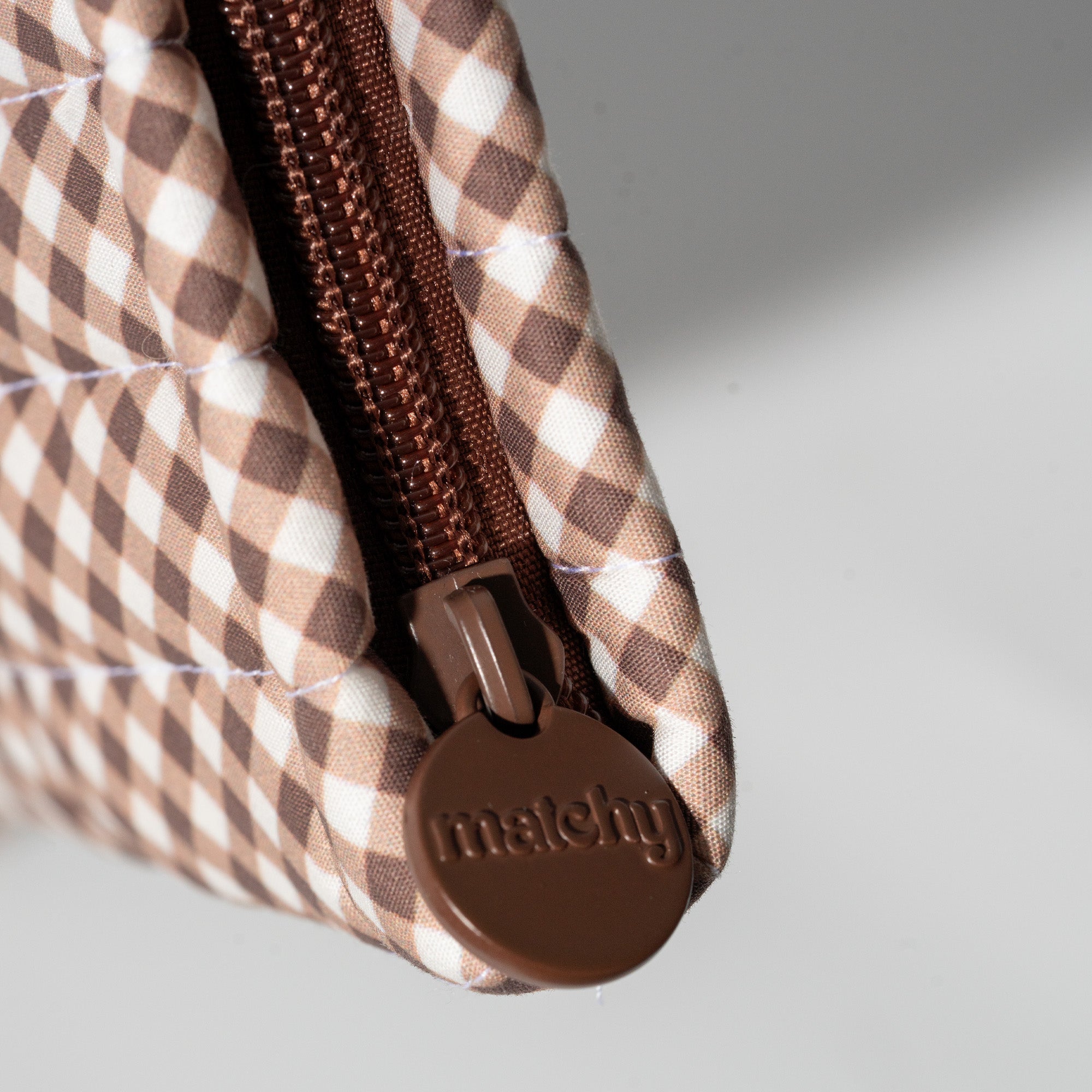 Close up of brown and cream gingham quilting with a brown zip and round brown 'matchy' zip pull. Matchy Chocolate Gingham Book Sleeve zip detail.
