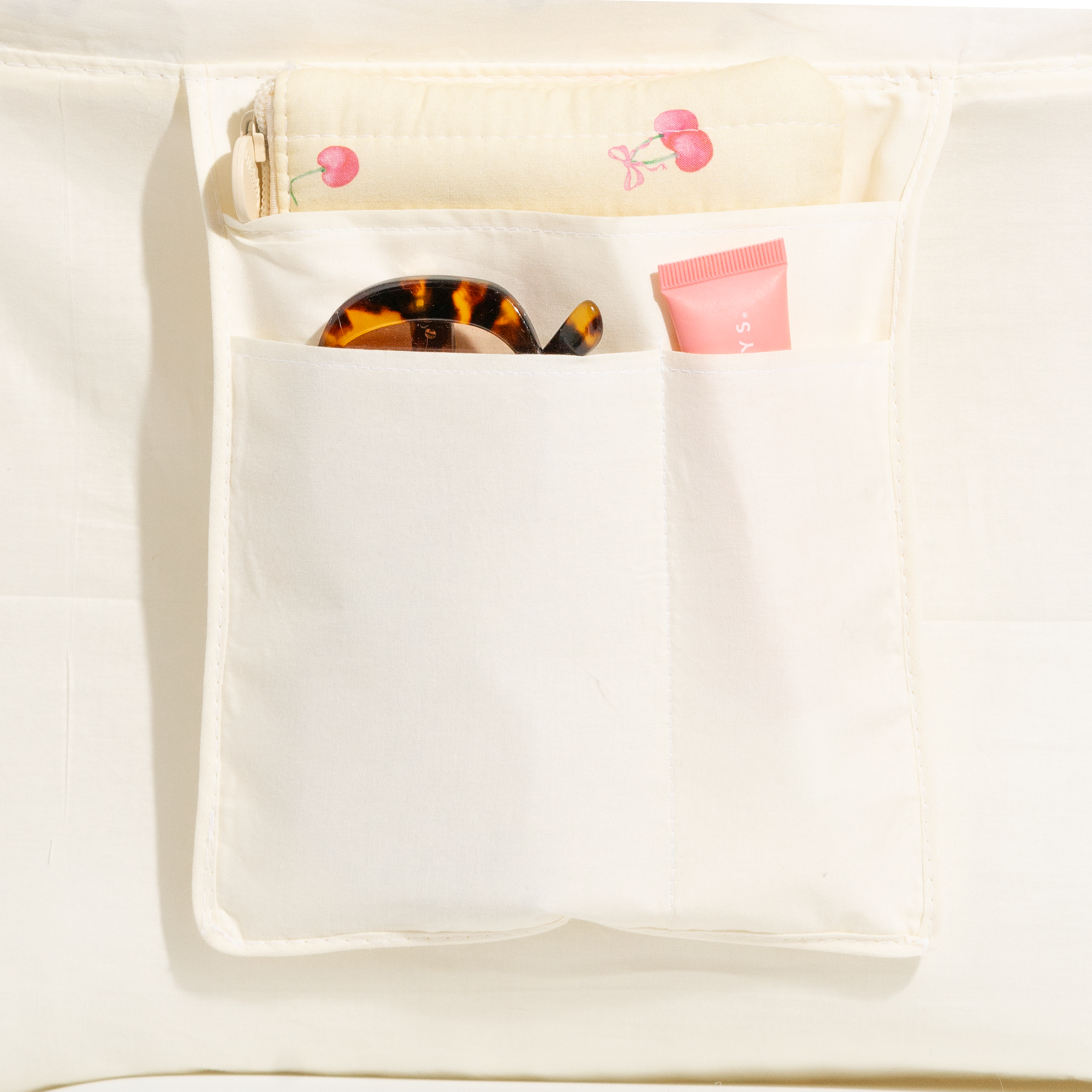 Close up of a cream tote lining with slip pockets holding a hair clip, lip balm and a cherry print pouch. Matchy Blueberry Take Me With You Tote interior pockets.