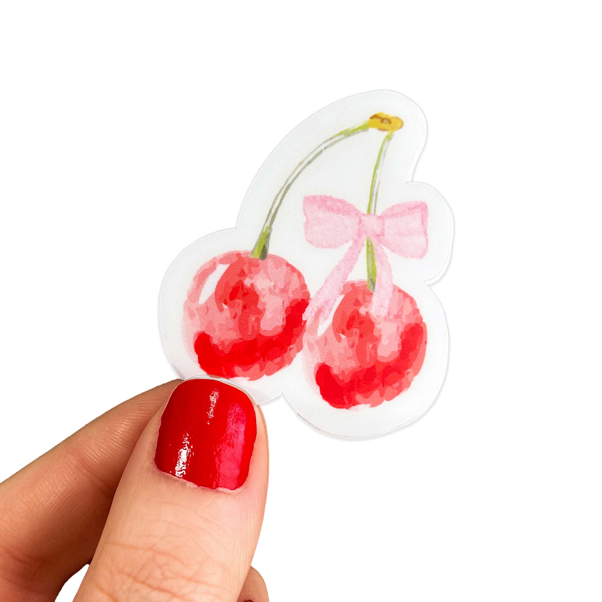 Hand with red nails holding a die cut sticker of two red cherries tied with a pink bow. Matchy Chérie Sticker.