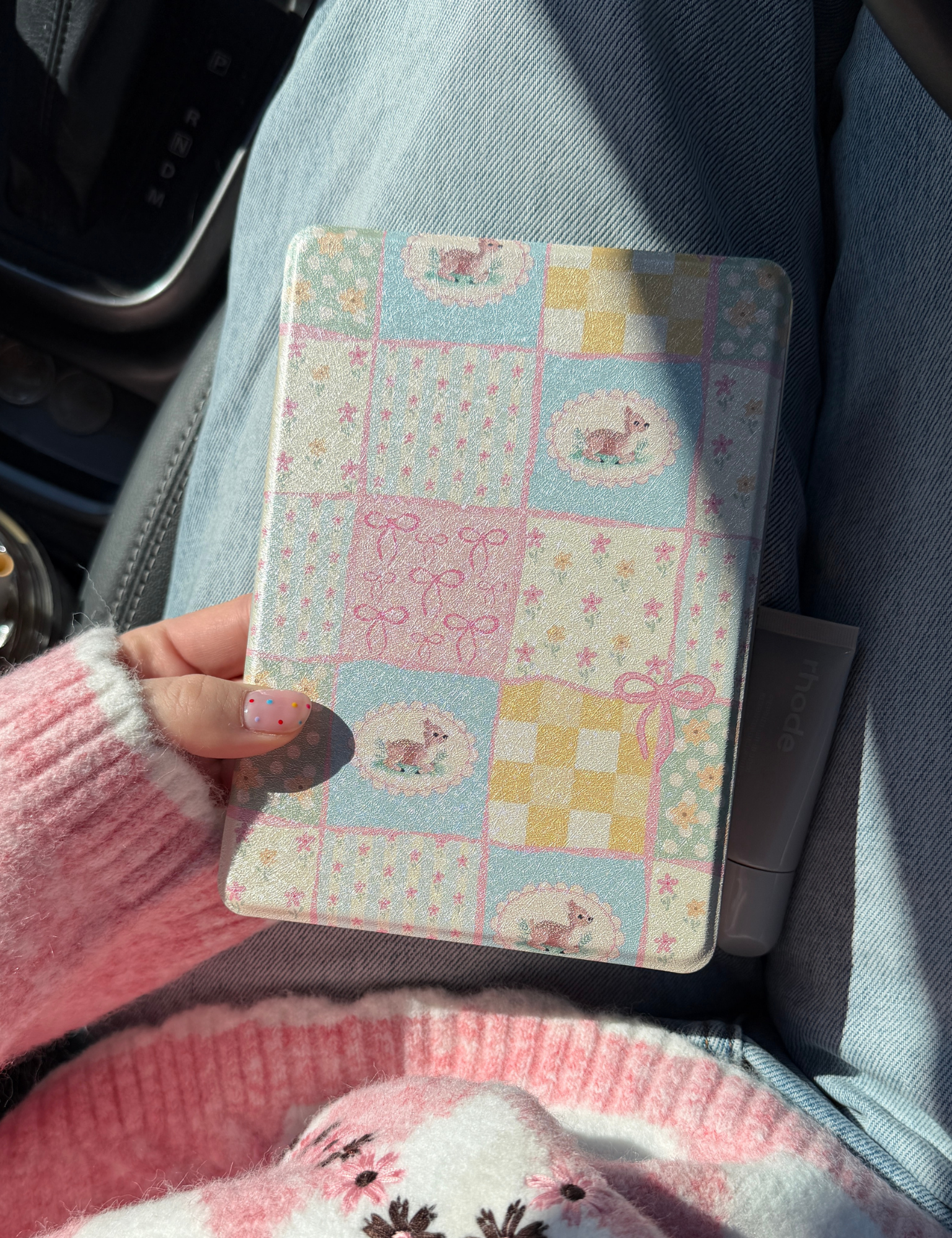 Hand holding a pastel patchwork print Kindle case with deer and bow motifs, in a car. Kindle Cover with Vegan Leather. Matchy Kindle cover for 6.8 inch Kindle with plastic back.
