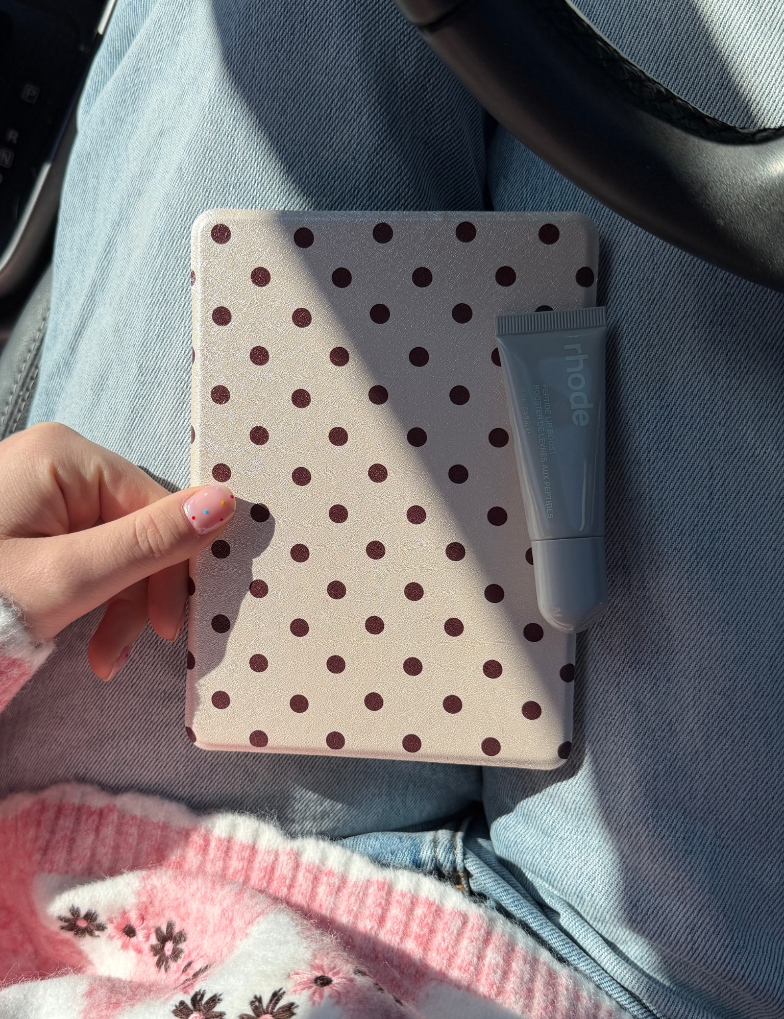 Hand holding a cream Kindle case with brown polka dots and a tube of lip balm on top, in a car. Kindle Cover with Vegan Leather. Matchy Kindle cover for 6.8 inch Kindle with plastic back.