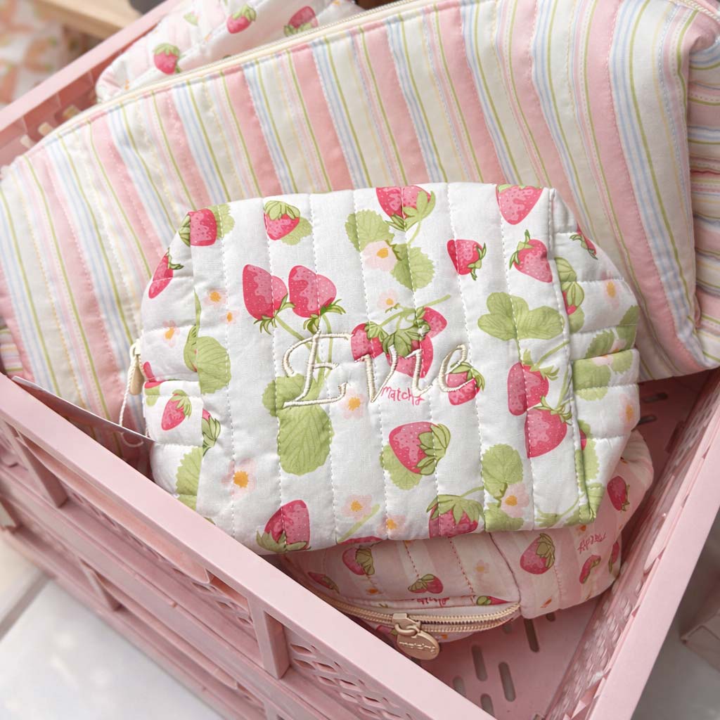 Strawberry print quilted carry-all bag embroidered with a name in cream script, sitting in a pink crate with striped bags. Matchy Sofia Custom Embroidery Carry-All Bag.